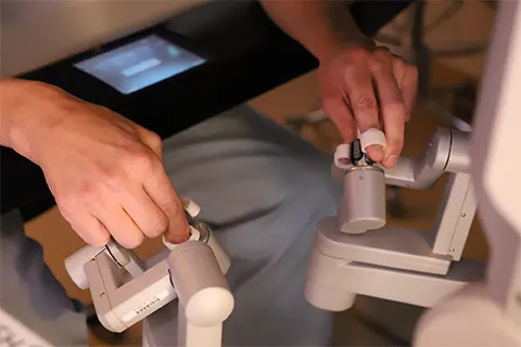 Photograph showing surgeons hands controlling the robotic machine.