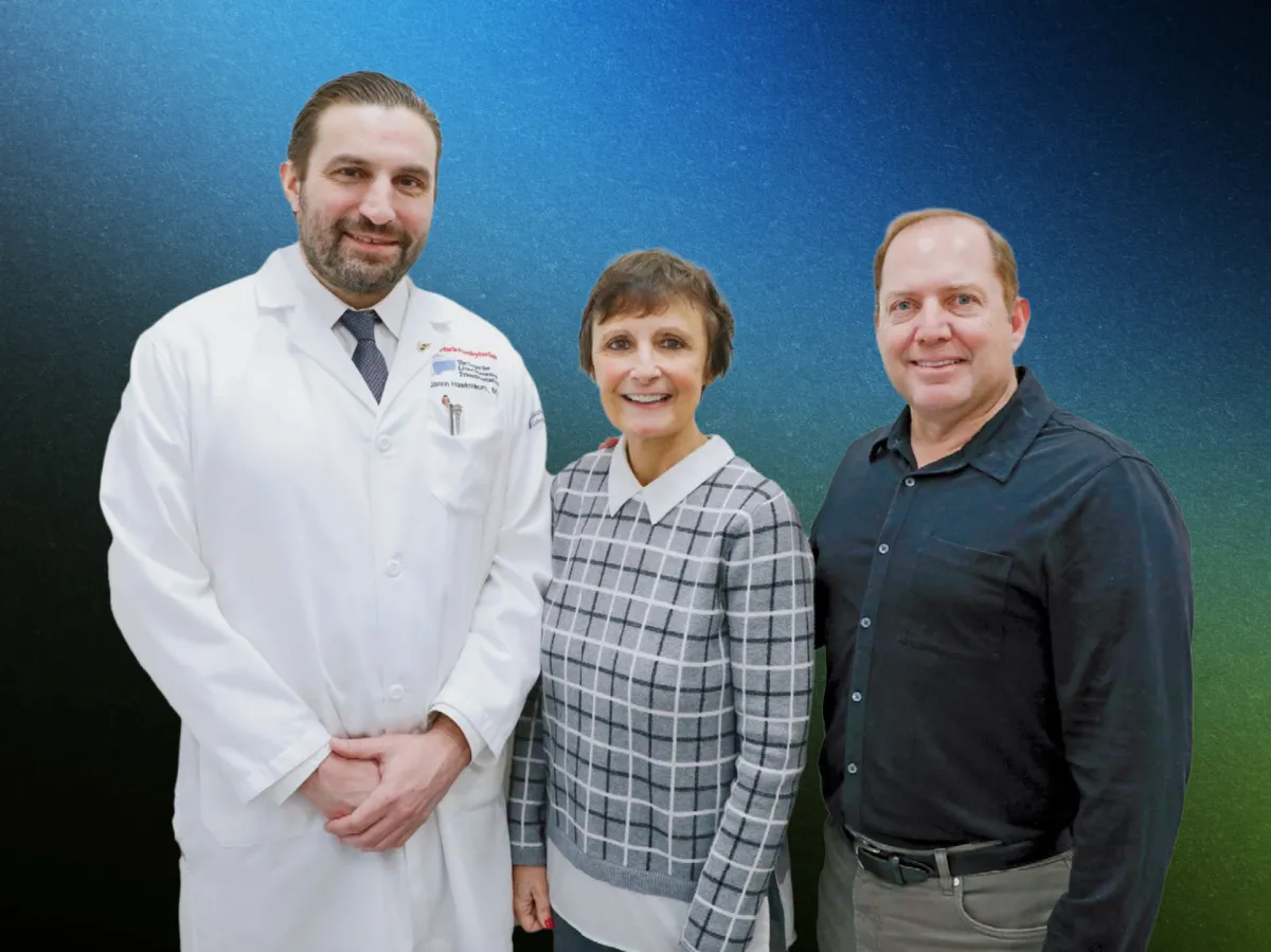 A surgeon stands with patient and patient's spouse