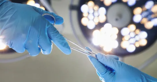 Close-up photo of a gloved hand exchanging surgical tools with another gloved hand.