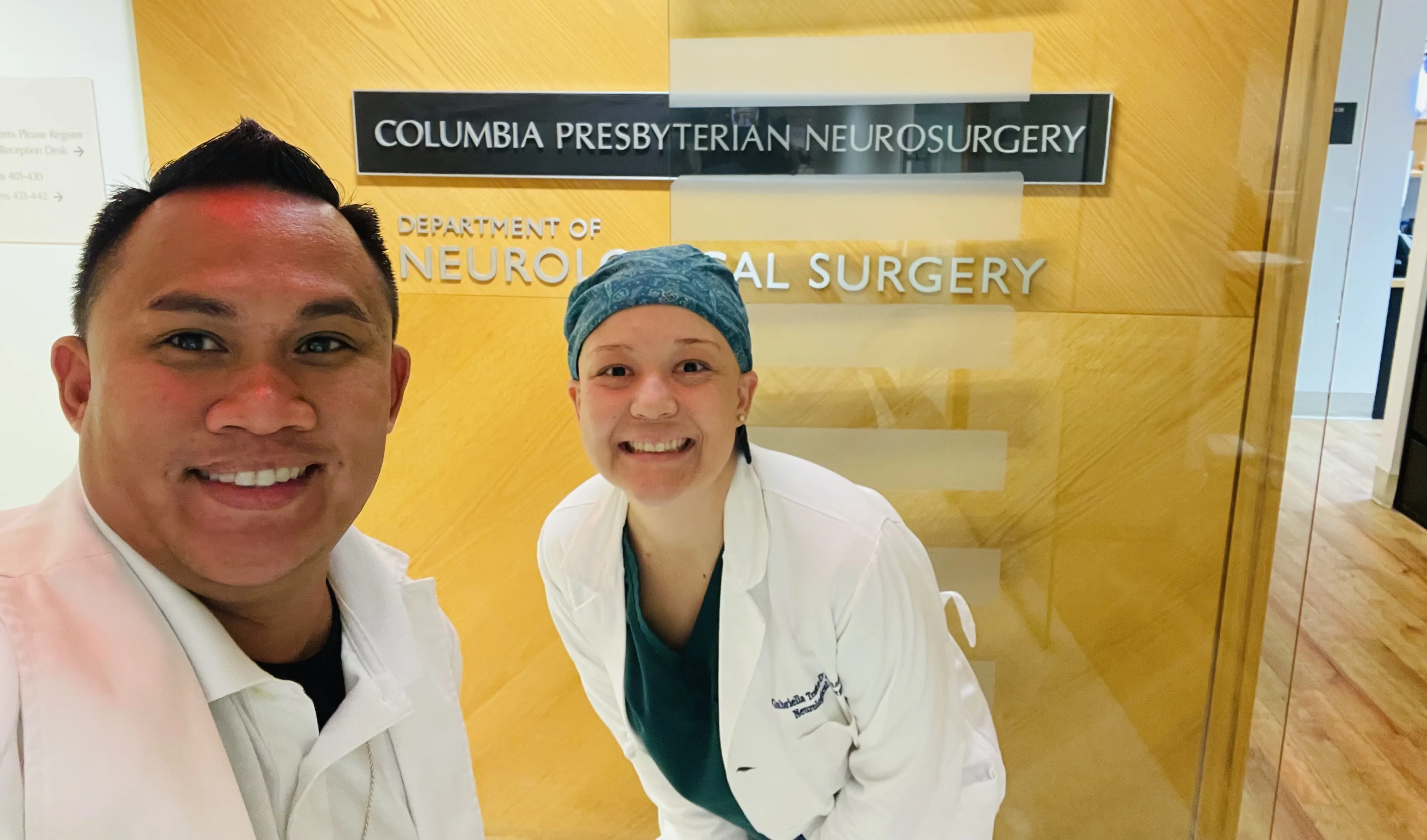 Gaby poses in front of neurosurgery sign with coworker
