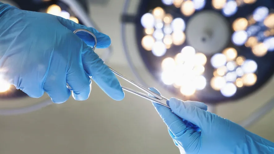 Close-up photo of a gloved hand exchanging surgical tools with another gloved hand.